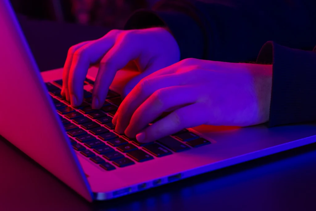 man uses laptop closeup male hands neon lighting